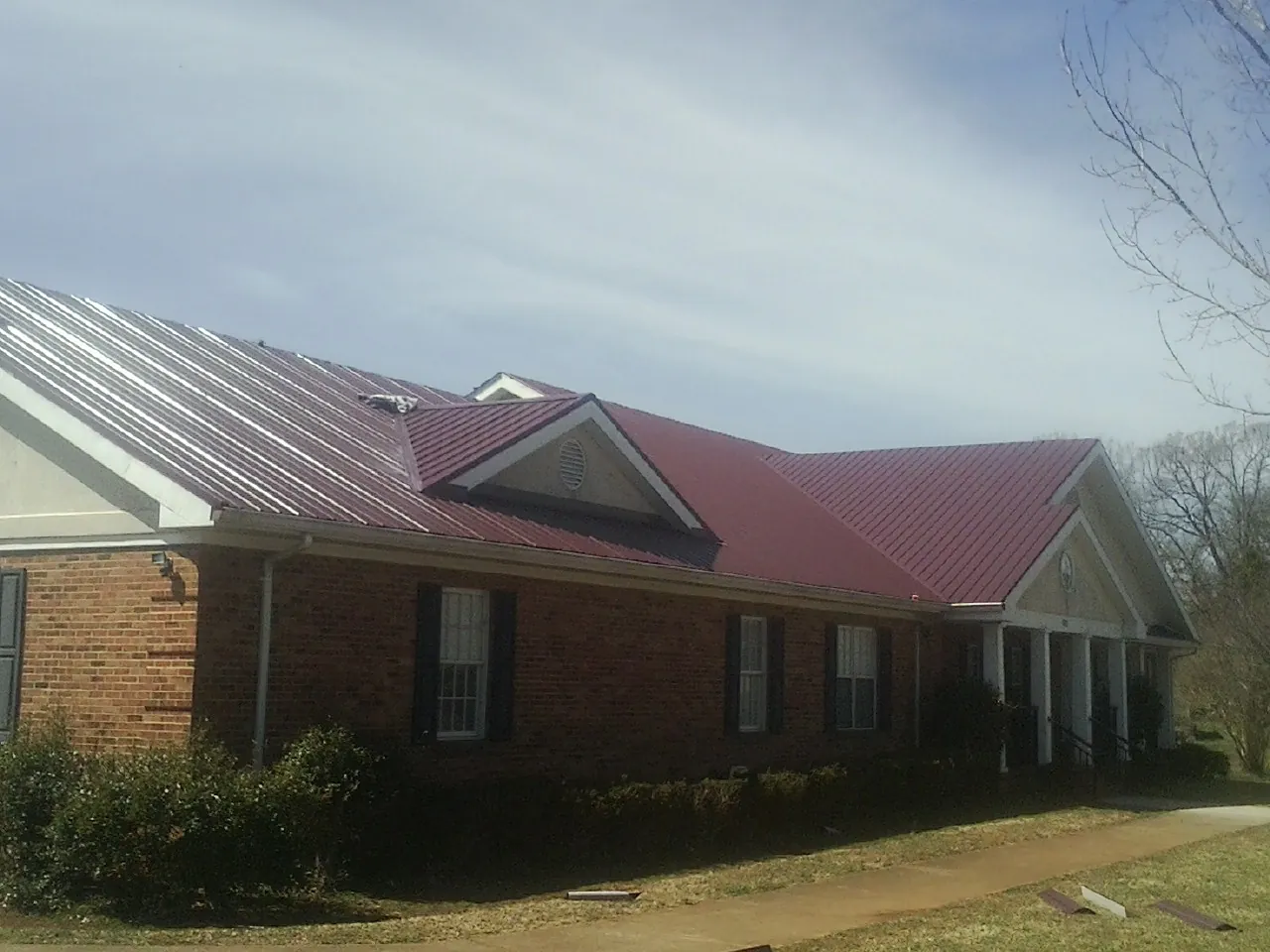 Red metal roof with gabled entries on a long brick building, from a Hail Damage Roof Repair job in Stanfordville