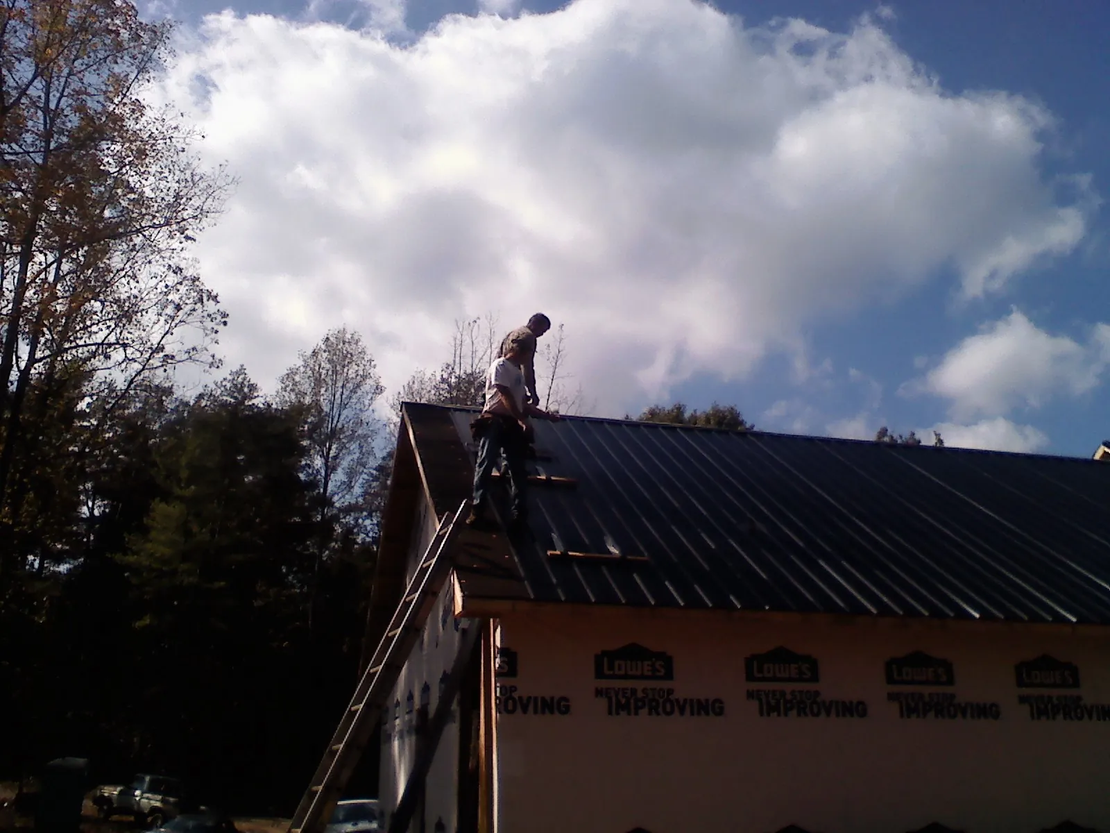 Roofer fastening dark metal panels high against a cloudy sky, from a Roof Inspection job in Stanfordville