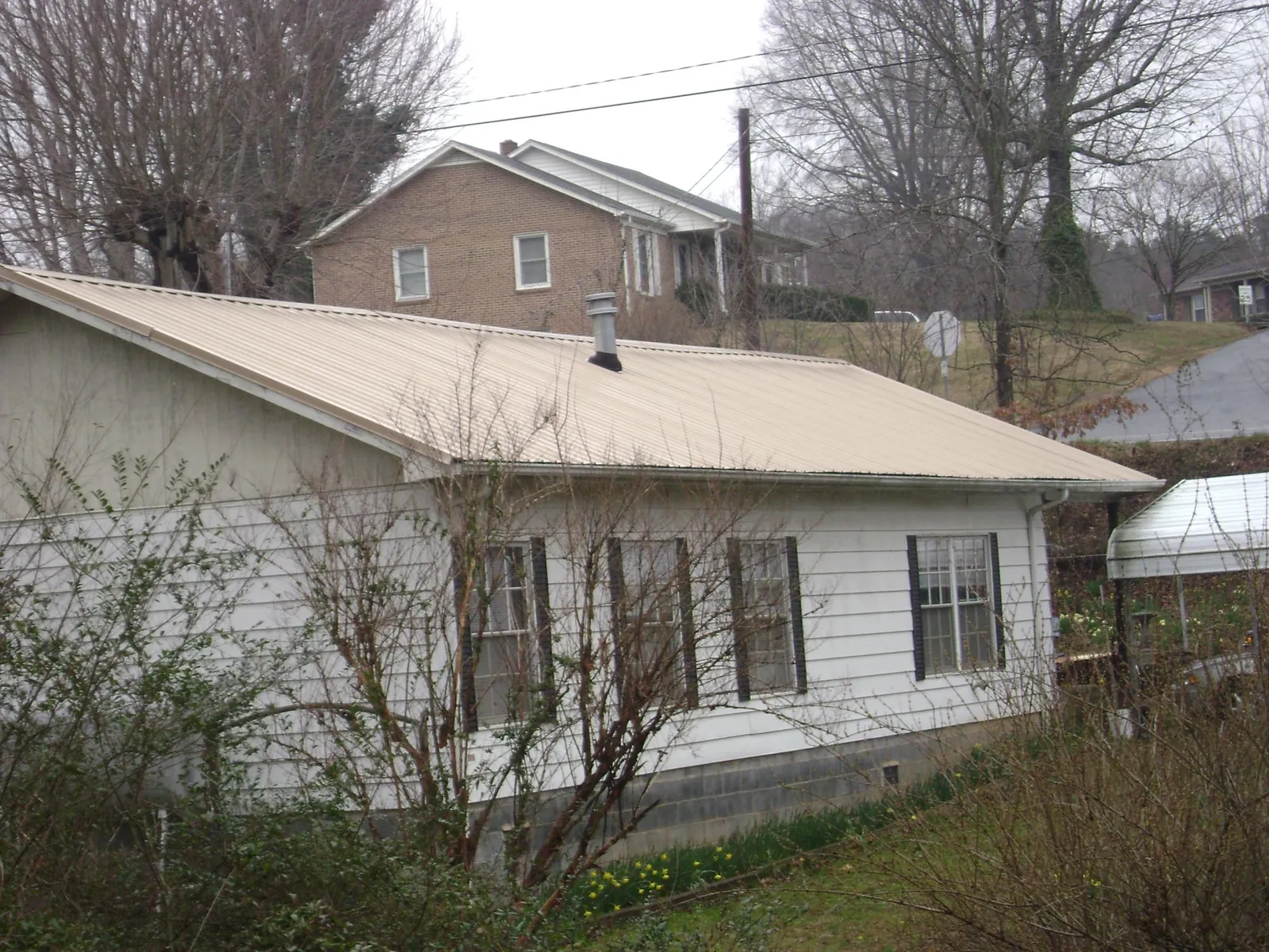 Tan metal roof on a white sided house set into a hillside — Commercial Roofing by Roofing Brothers in Stanfordville